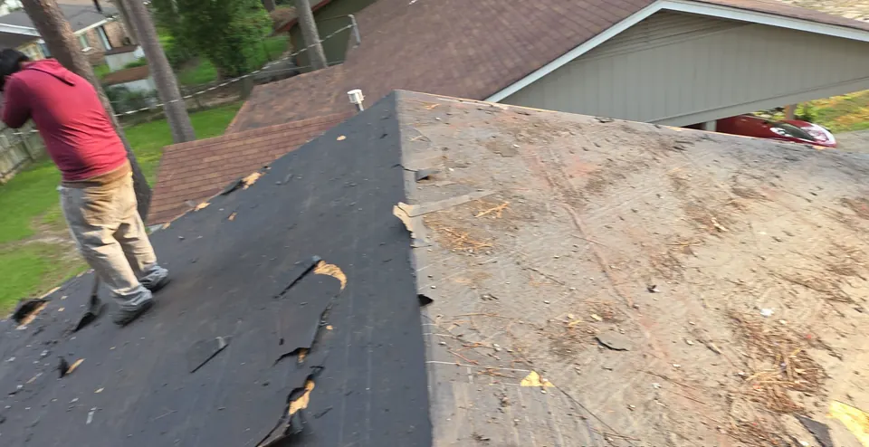 A Patriot Roofing crew member tearing off old shingles down to the roof deck