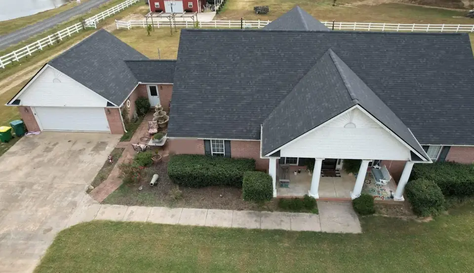 Drone view of a brick country home with a new charcoal shingle roof and white porch columns