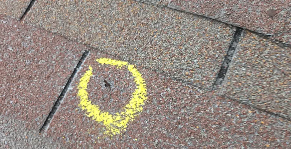 A hail hit on an asphalt shingle circled in yellow chalk during a storm damage inspection