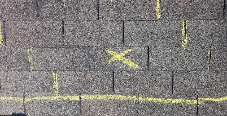 Chalk lines marking a test square and hail hits on a shingle roof during an insurance inspection