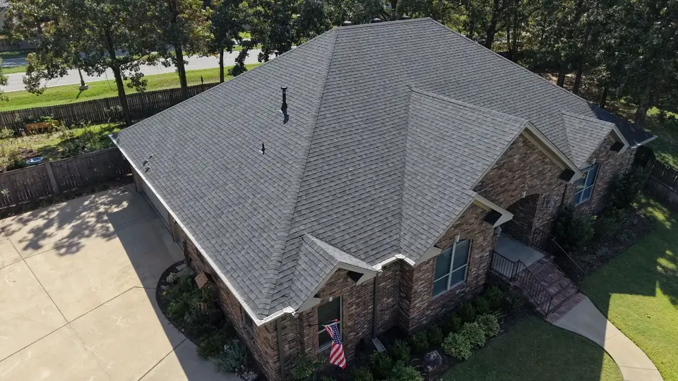 Aerial view of a new gray shingle roof on a brick home in Maumelle, with an American flag by the front window