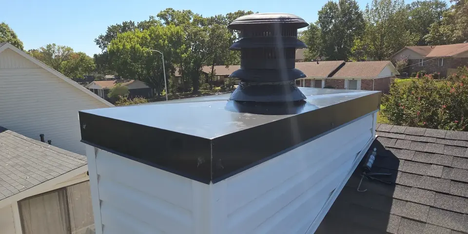 A new black metal chimney cap on a white chimney chase above a shingle roof in Sherwood