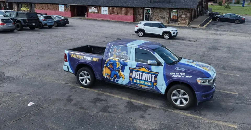 The wrapped Patriot Roofing pickup parked at a commercial roofing job