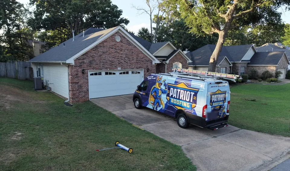 A wrapped Patriot Roofing van in a homeowner driveway with ladders on the roof rack