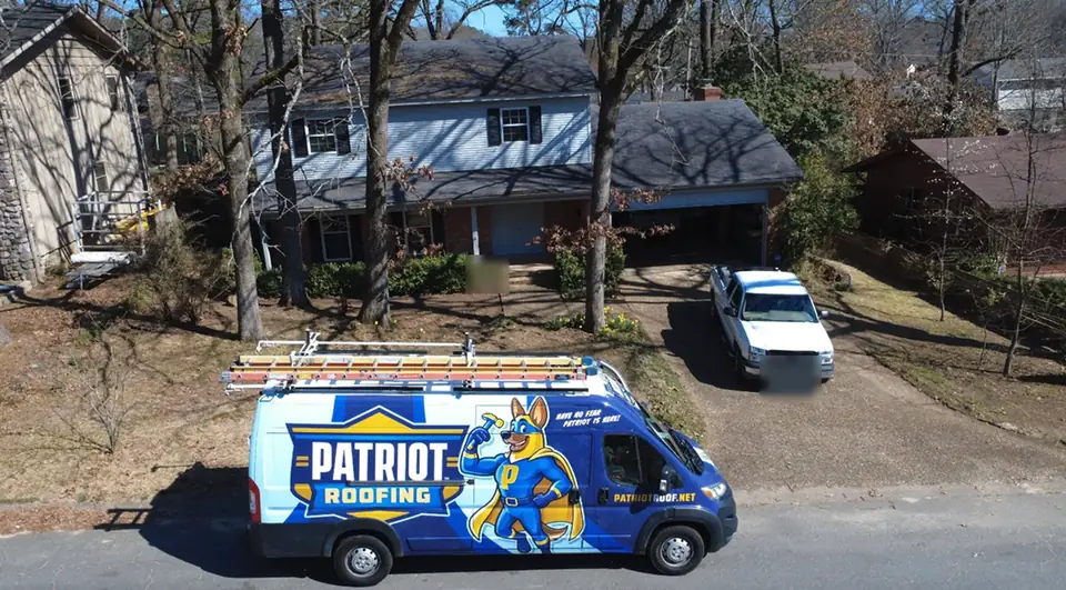 A wrapped Patriot Roofing van parked in front of a two-story home with ladders on the roof rack