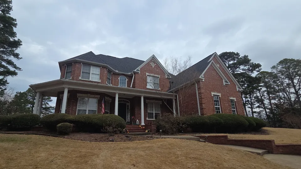 A two-story red brick home in West Little Rock with a dark shingle roof and a wraparound front porch