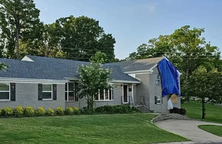 Home with a blue tarp over storm damage on the roof